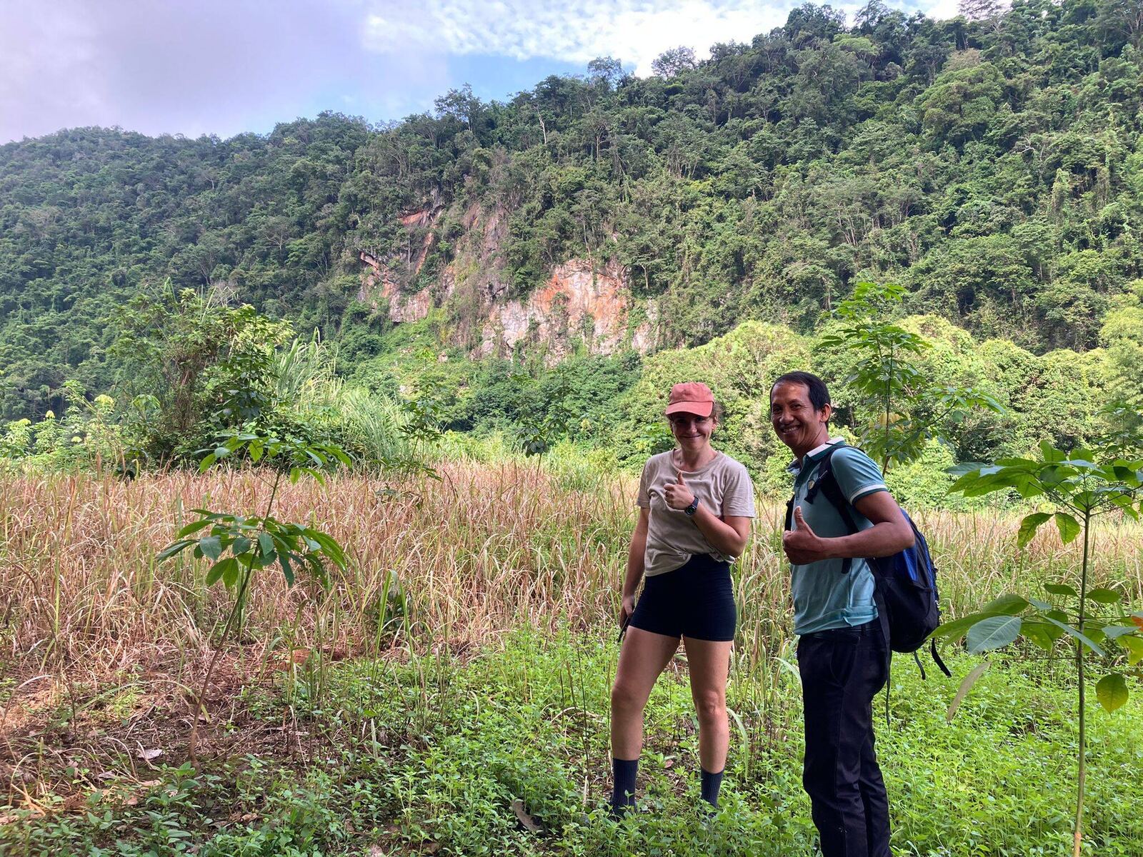 A guide and a guest on a trail below a forested cliff